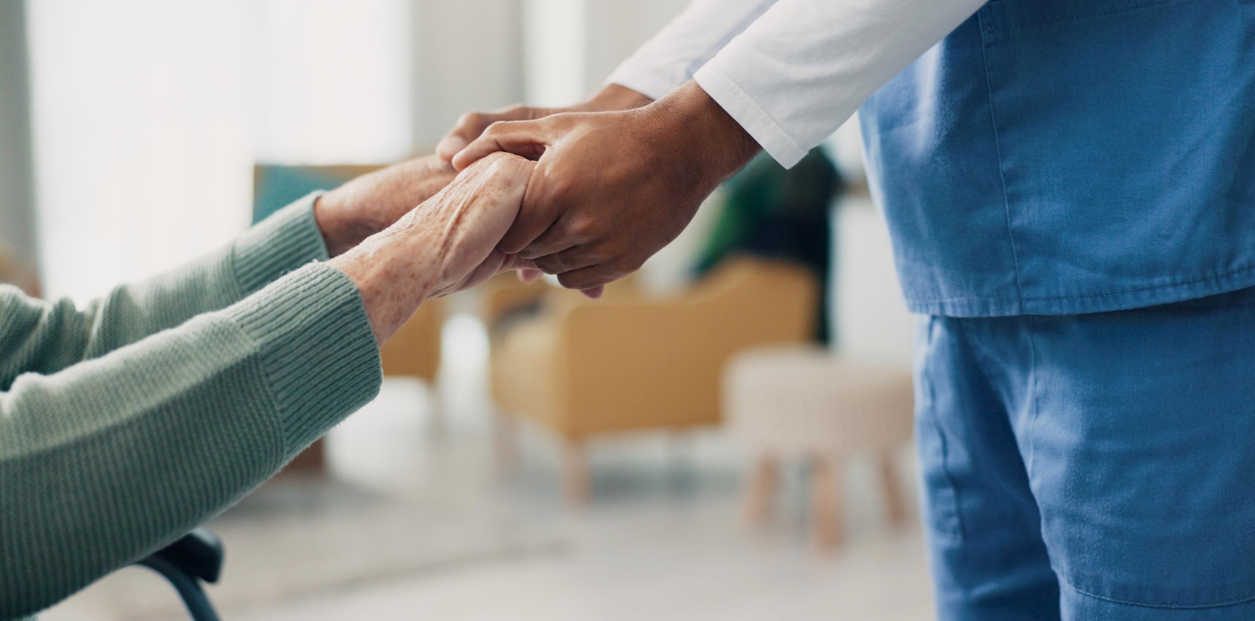 Ældre person og plejer holder hinanden i hænderne