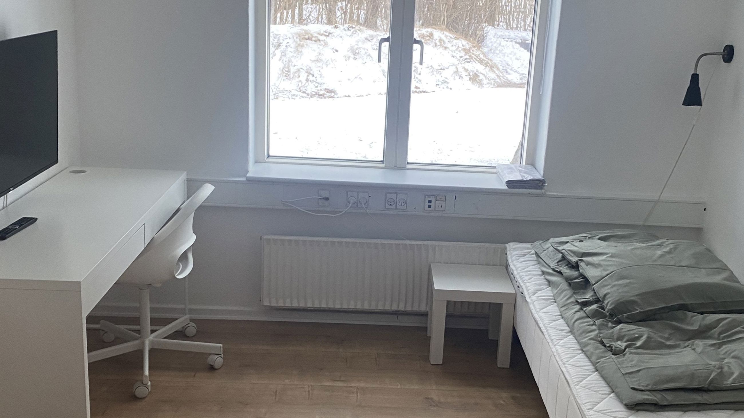 Værelse med seng, skrivebord, stol og computerskærm