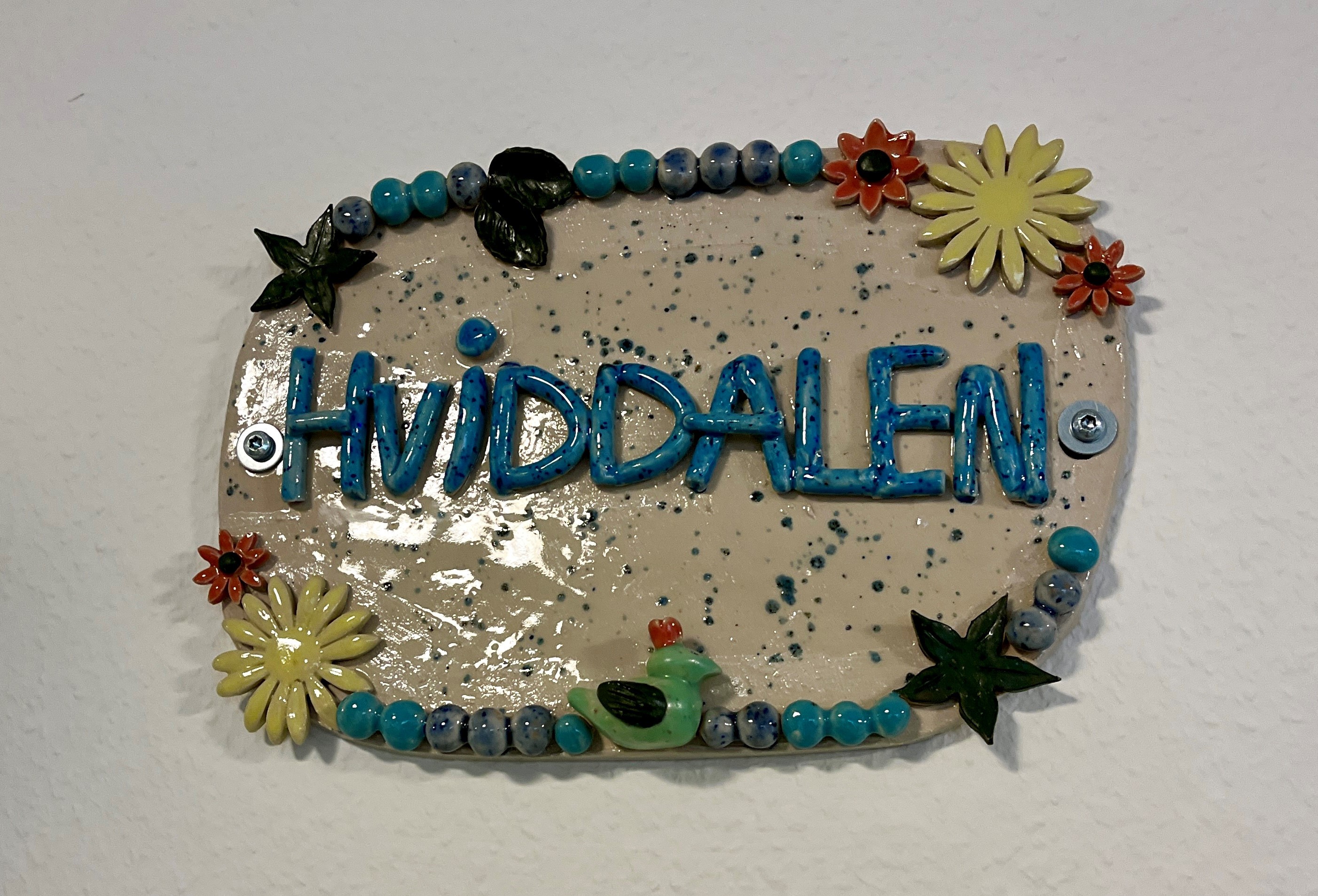 Keramisk skilt med teksten "Hviddalen" og blomster på
