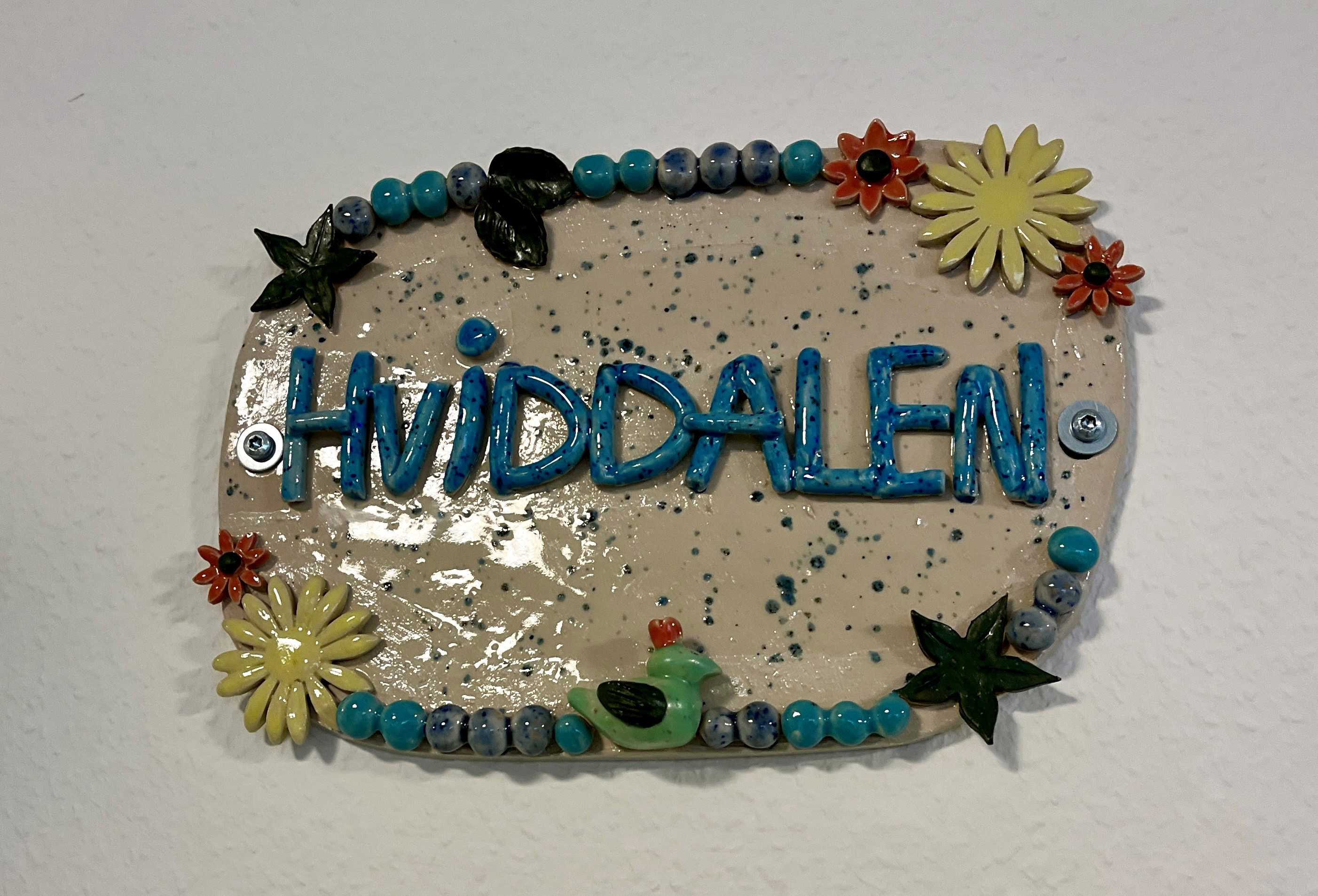 Keramisk skilt med teksten "Hviddalen" og blomster på