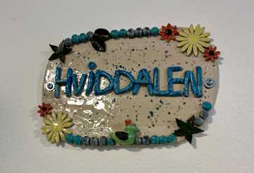 Keramisk skilt med teksten "Hviddalen" og blomster på